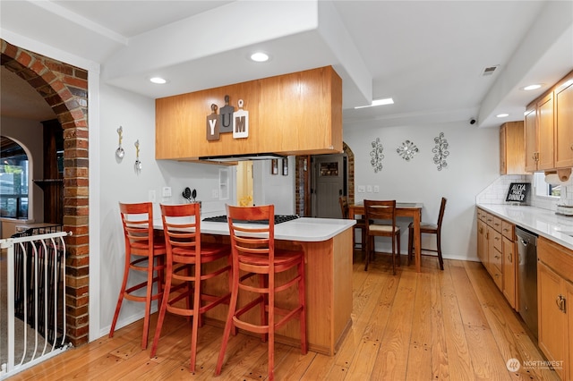 kitchen featuring light wood-style flooring, a peninsula, light countertops, stainless steel dishwasher, and backsplash