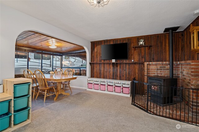 living room featuring carpet, a wood stove, wood walls, and a textured ceiling