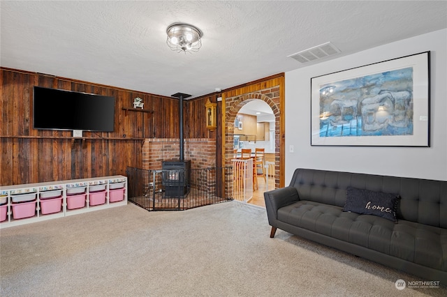 carpeted living area featuring arched walkways, a wood stove, visible vents, and wood walls