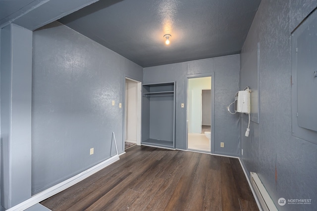 unfurnished bedroom with electric panel, a baseboard radiator, a wall mounted AC, dark hardwood / wood-style floors, and a closet