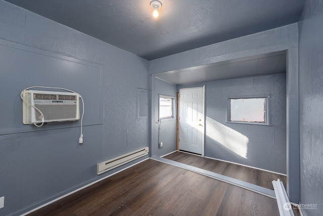 empty room with dark wood-type flooring, a wall unit AC, and baseboard heating