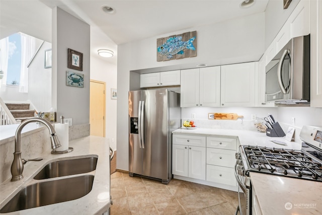 kitchen with stainless steel appliances, sink, light tile patterned floors, light stone countertops, and white cabinetry