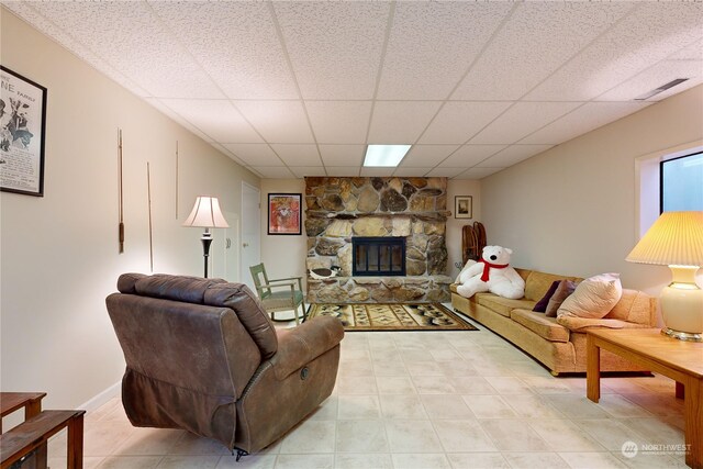 living room featuring a paneled ceiling and a stone fireplace