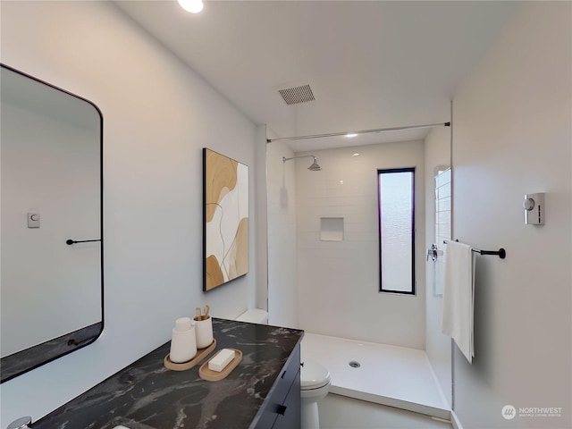 bathroom with a tile shower, vanity, and toilet