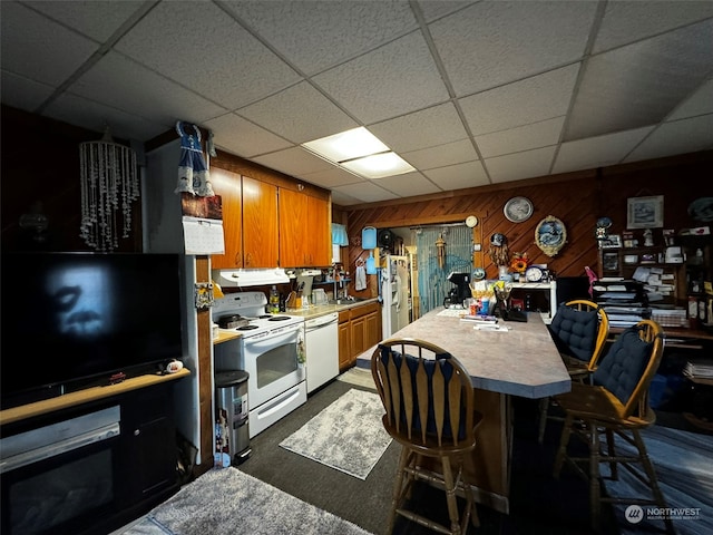 kitchen featuring white appliances, wooden walls, sink, a breakfast bar, and a drop ceiling