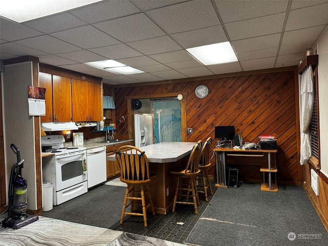 kitchen featuring white appliances, a paneled ceiling, and wooden walls