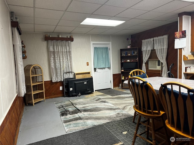 dining space with wood walls, concrete floors, cooling unit, and a drop ceiling