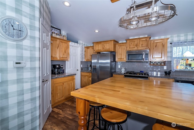 kitchen with butcher block counters, backsplash, appliances with stainless steel finishes, dark hardwood / wood-style floors, and a breakfast bar area