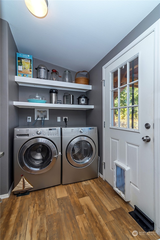 clothes washing area with washer and clothes dryer, heating unit, and wood-type flooring