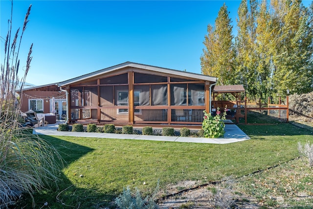 rear view of property featuring a lawn, a sunroom, and a patio