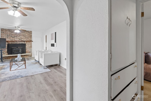 interior space featuring light wood-type flooring, ceiling fan, and a wood stove