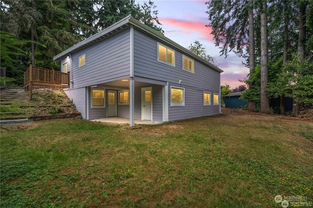 back house at dusk featuring a wooden deck, a patio, and a yard