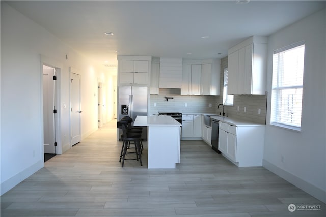 kitchen with a breakfast bar area, a center island, white cabinets, stainless steel appliances, and backsplash