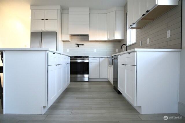 kitchen with appliances with stainless steel finishes, white cabinets, decorative backsplash, light hardwood / wood-style floors, and wall chimney exhaust hood