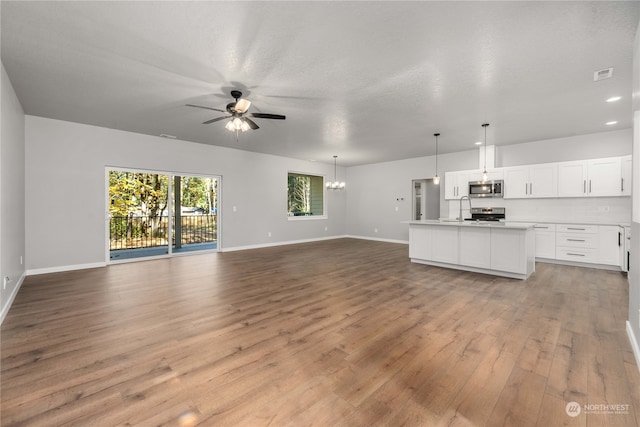 unfurnished living room with a textured ceiling, sink, light hardwood / wood-style floors, and ceiling fan with notable chandelier