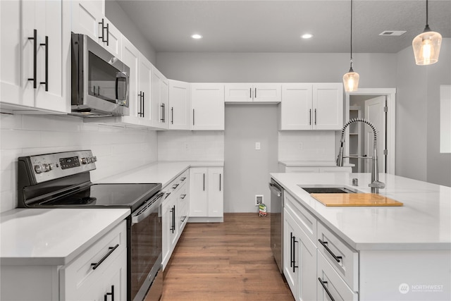 kitchen with appliances with stainless steel finishes, decorative light fixtures, a center island with sink, and white cabinets