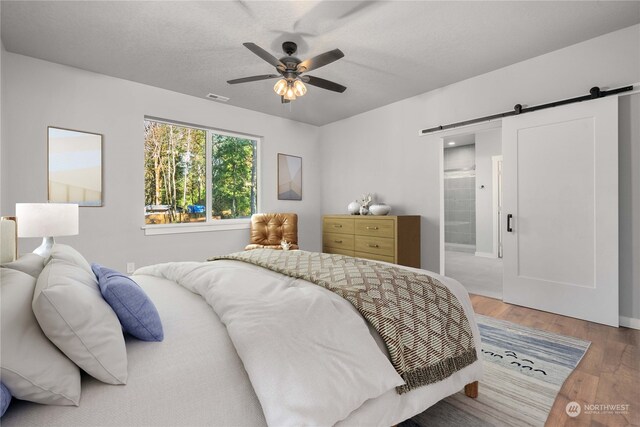 bedroom featuring hardwood / wood-style flooring, a textured ceiling, a barn door, connected bathroom, and ceiling fan