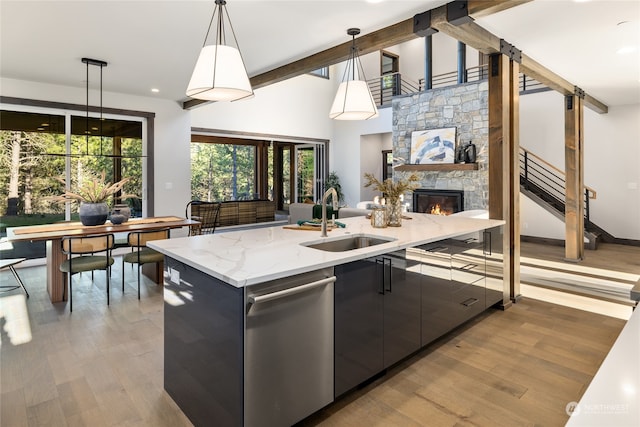 kitchen with a stone fireplace, sink, stainless steel dishwasher, light stone countertops, and decorative light fixtures