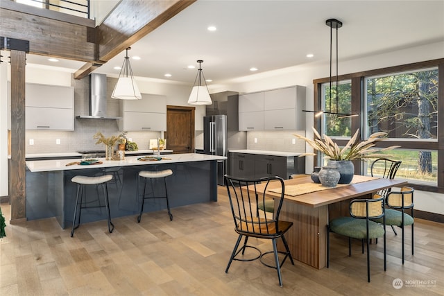 kitchen featuring wall chimney exhaust hood, hanging light fixtures, a kitchen bar, gray cabinets, and a center island with sink