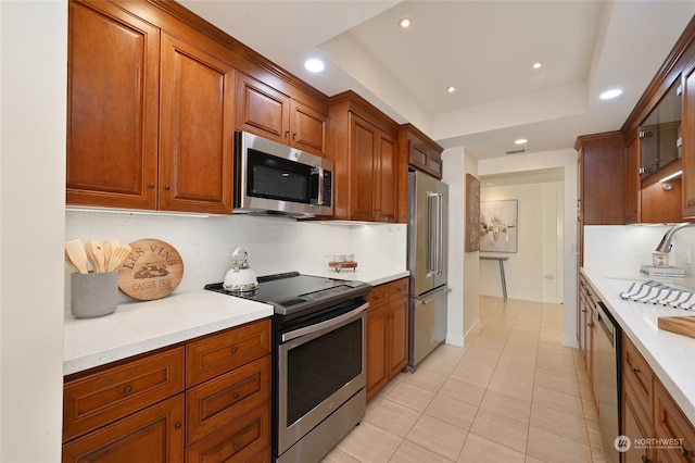 kitchen with a tray ceiling, appliances with stainless steel finishes, light stone counters, and light tile patterned flooring