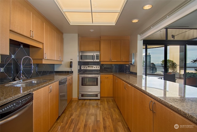 kitchen featuring stainless steel appliances, stone countertops, sink, backsplash, and light hardwood / wood-style flooring