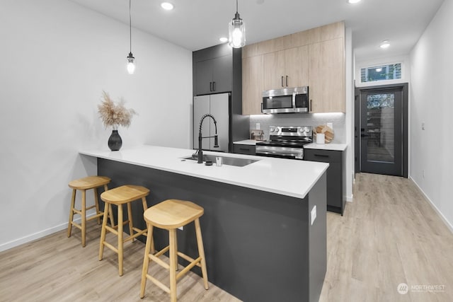 kitchen featuring light brown cabinetry, light wood-type flooring, a breakfast bar, stainless steel appliances, and hanging light fixtures