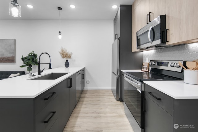 kitchen with kitchen peninsula, appliances with stainless steel finishes, sink, pendant lighting, and light hardwood / wood-style flooring