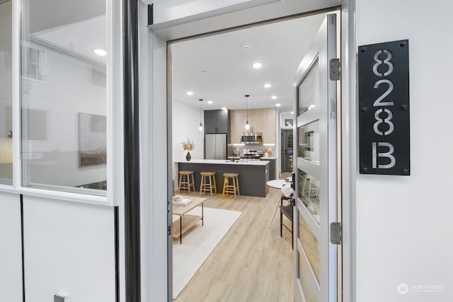 interior space featuring decorative light fixtures, a kitchen island, light wood-type flooring, and stainless steel appliances