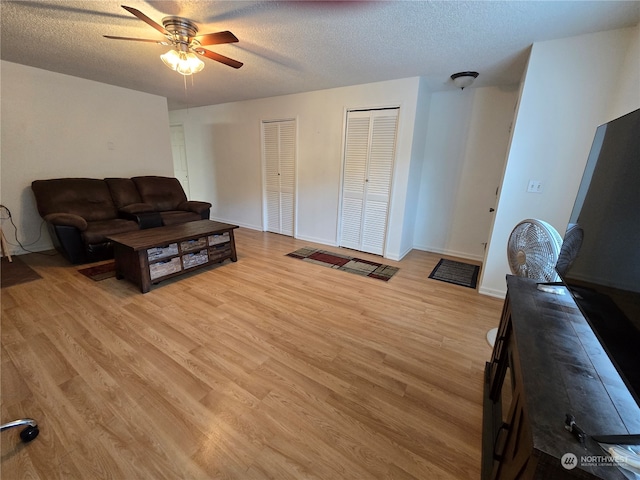 living room with light hardwood / wood-style flooring, a textured ceiling, and ceiling fan