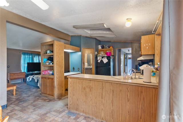 kitchen featuring vaulted ceiling, black refrigerator, kitchen peninsula, a textured ceiling, and sink