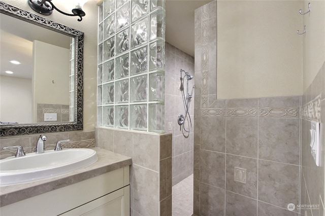 bathroom with a tile shower, vanity, and tile walls