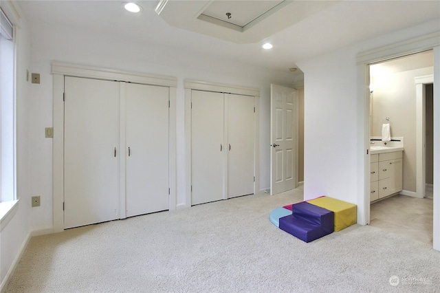 unfurnished bedroom featuring light carpet, ensuite bathroom, and multiple closets