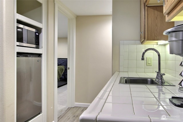 kitchen with decorative backsplash, light wood-type flooring, stainless steel appliances, sink, and tile countertops