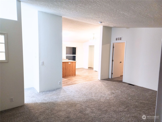 carpeted spare room featuring a textured ceiling, lofted ceiling, and a notable chandelier