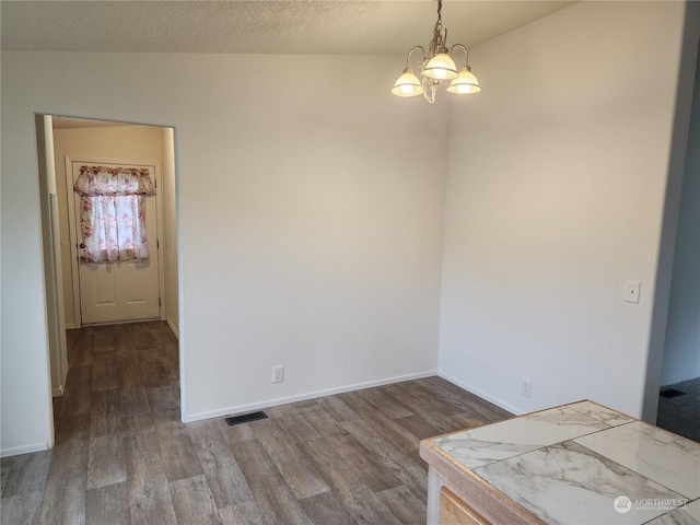 unfurnished dining area with vaulted ceiling, a chandelier, a textured ceiling, and wood-type flooring