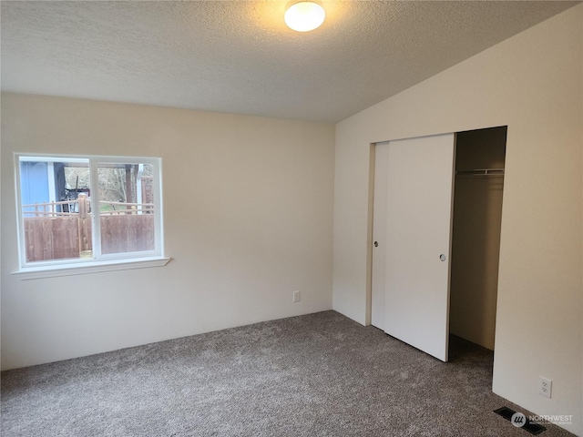 unfurnished bedroom featuring a textured ceiling, dark carpet, and a closet