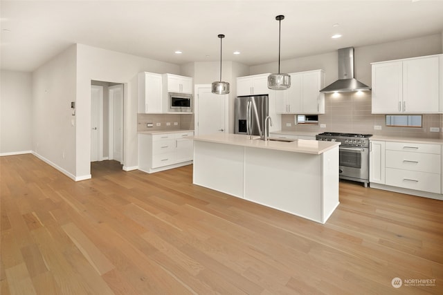 kitchen featuring appliances with stainless steel finishes, a kitchen island with sink, sink, white cabinets, and wall chimney exhaust hood