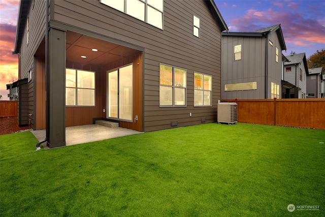 back house at dusk featuring a yard, a patio, and central AC