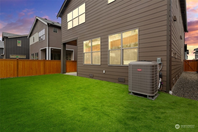 back house at dusk with central air condition unit and a lawn