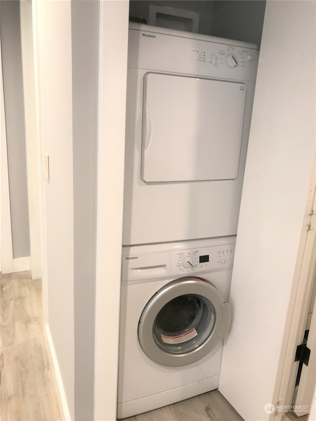 clothes washing area with light hardwood / wood-style flooring and stacked washer / drying machine