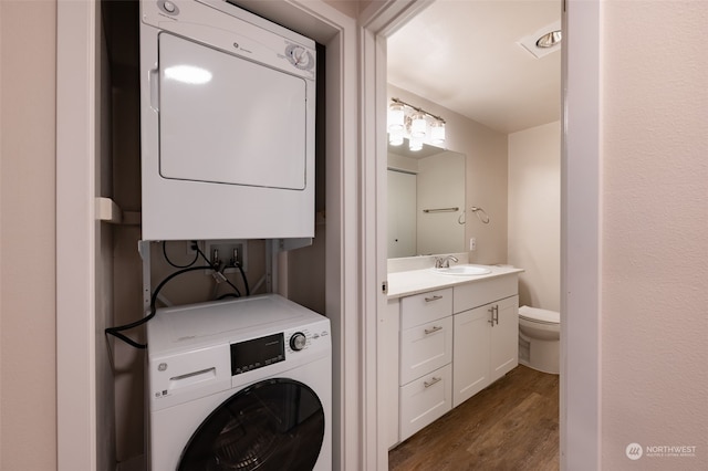 clothes washing area with dark wood-type flooring, sink, and stacked washer / dryer