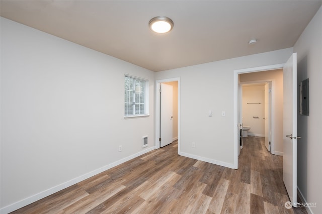 unfurnished bedroom featuring connected bathroom, electric panel, and light hardwood / wood-style floors