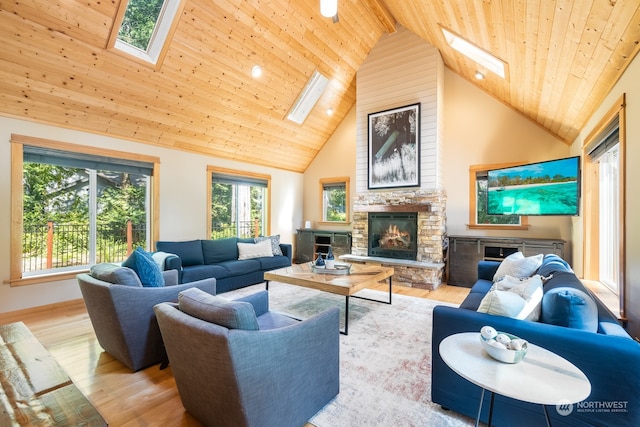 living room featuring beam ceiling, high vaulted ceiling, a skylight, a stone fireplace, and light wood-type flooring