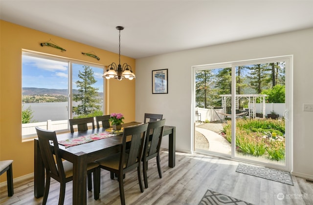 dining room with light hardwood / wood-style flooring, a water view, and a notable chandelier