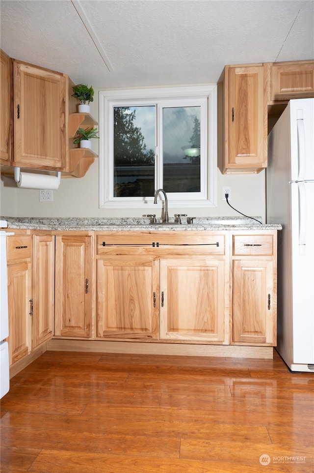 kitchen with light brown cabinetry, white refrigerator, sink, and light hardwood / wood-style flooring