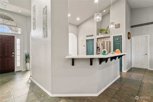 kitchen featuring a breakfast bar, kitchen peninsula, hanging light fixtures, a towering ceiling, and stainless steel fridge