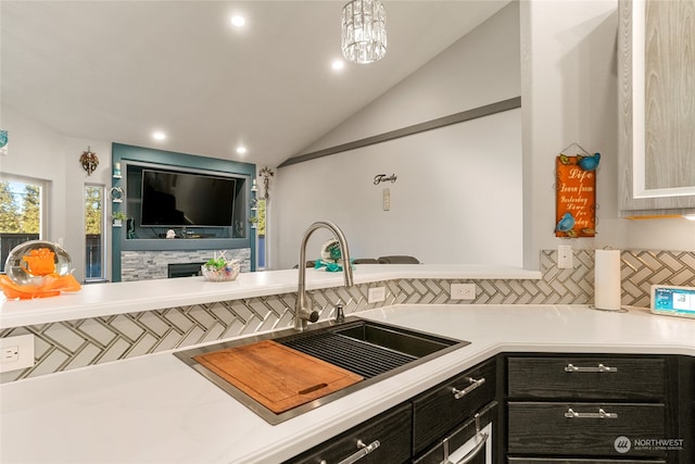 kitchen featuring a stone fireplace, lofted ceiling, decorative backsplash, sink, and pendant lighting