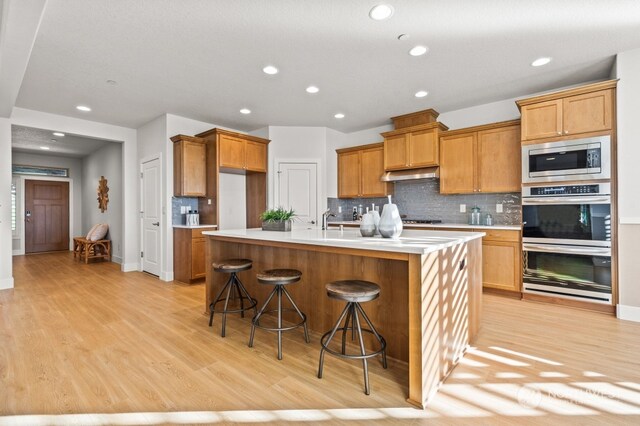 kitchen featuring sink, light hardwood / wood-style flooring, an island with sink, appliances with stainless steel finishes, and a breakfast bar area