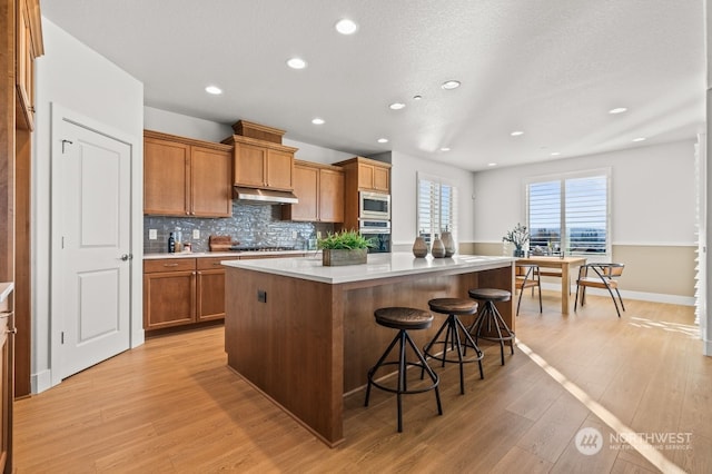 kitchen with a center island, stainless steel appliances, a kitchen breakfast bar, backsplash, and light hardwood / wood-style floors