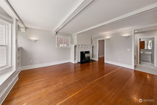 unfurnished living room featuring hardwood / wood-style flooring, a healthy amount of sunlight, and beam ceiling